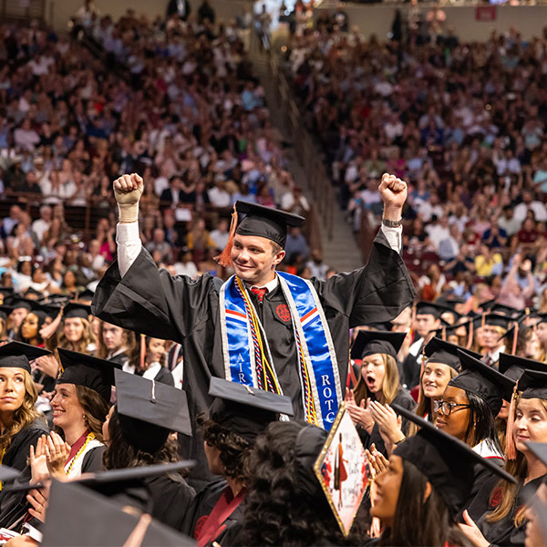 Student in cap and gown stands with fists raised in the air