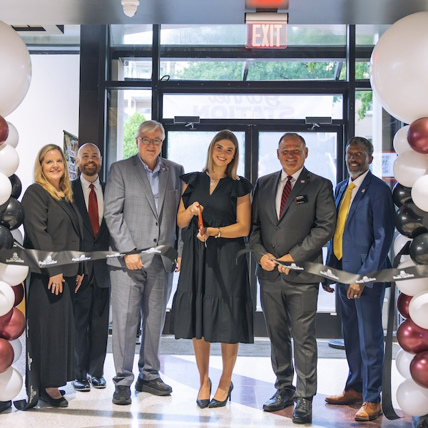 group of people under a garnet and black balloon arch cut a ribbon in a new dining facility