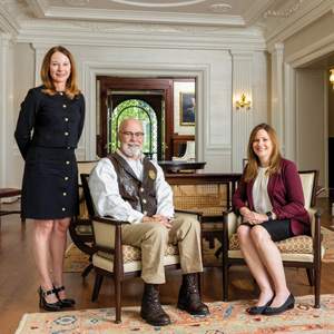 University of South Carolina School of Law alumni Emily Farr, left, Thomas Mullikin and Dolly Garfield pose in a formal room with wood floors, a fireplace and ornate light fixtures.